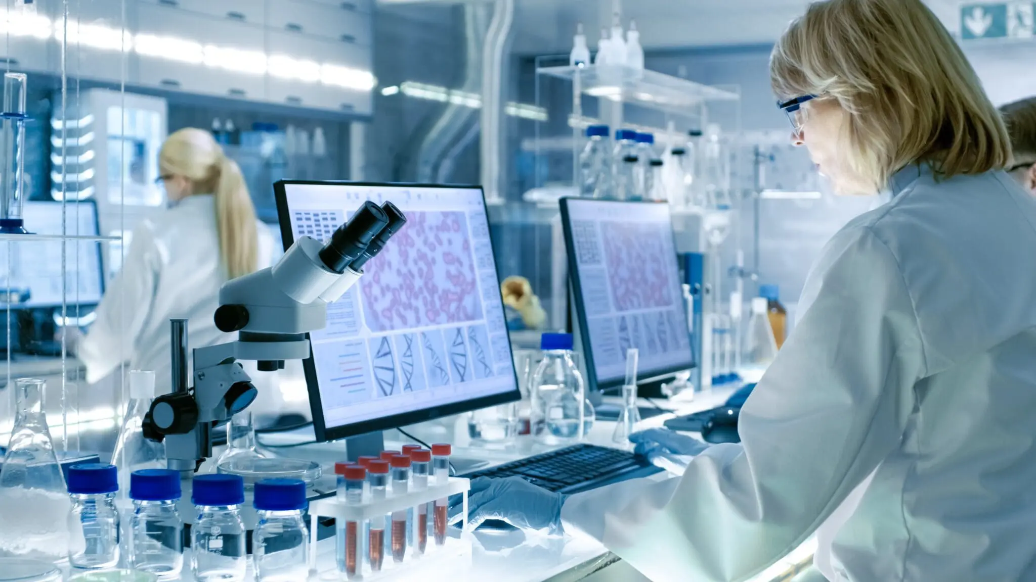 Senior Female Scientist Works with High Tech Equipment in a Modern Laboratory. Her Colleagues are Working Beside Her.